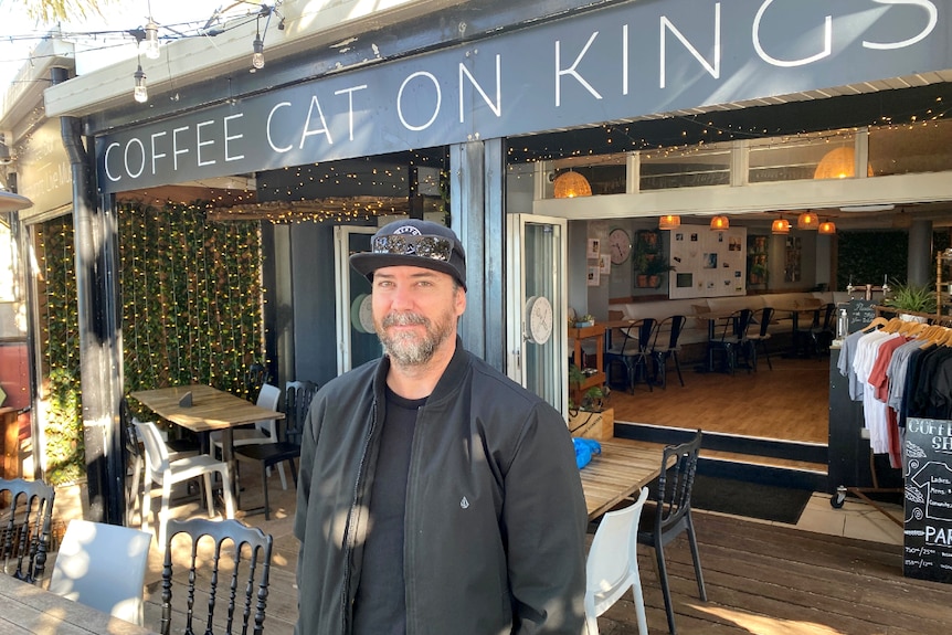 Man stands in front of coffee shop not smiling