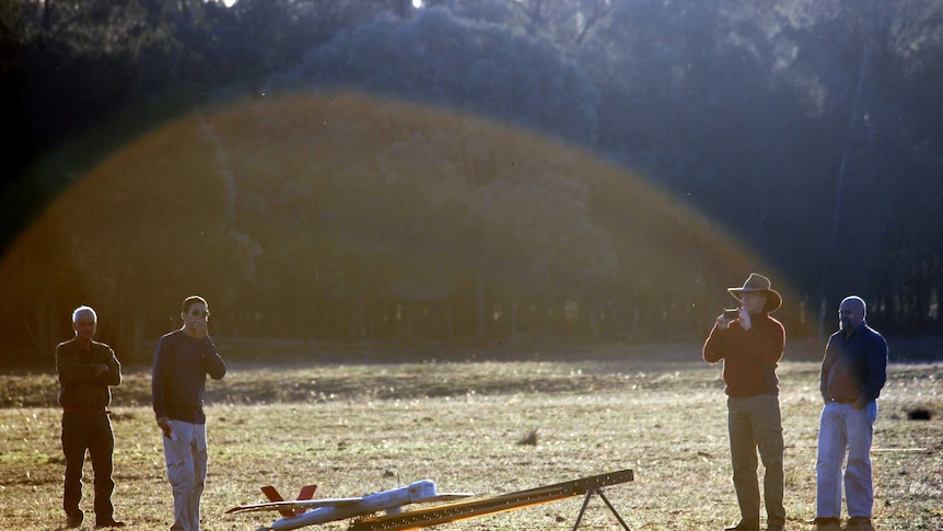 A military grade drone in a paddock in southern Queensland with four bystanders in the sunlight.