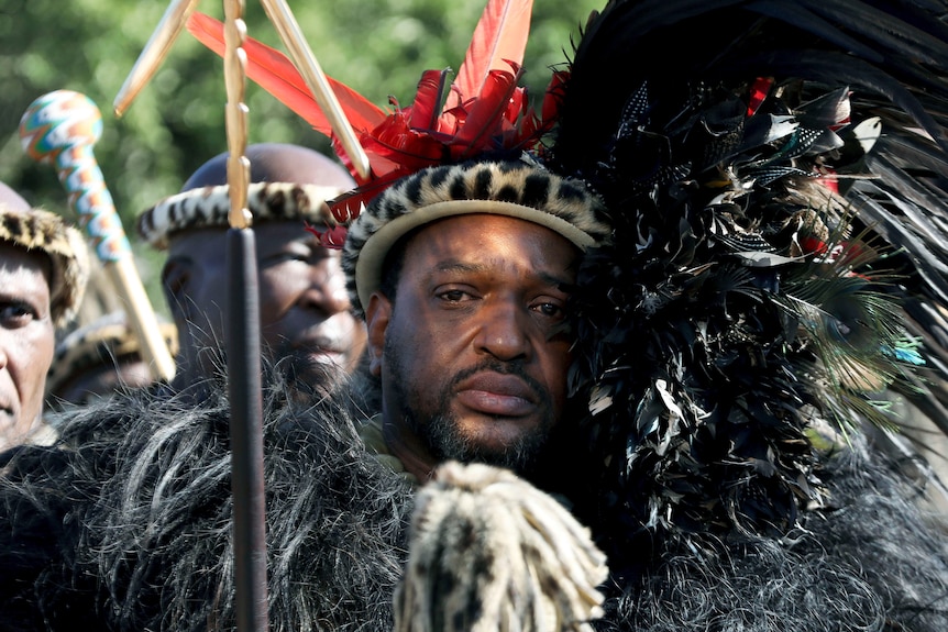 El rey Misuzulu ka Zwelithini lleva una diadema con estampado de leopardo y un traje tradicional zulú.  Los hombres detrás de él usan lo mismo. 