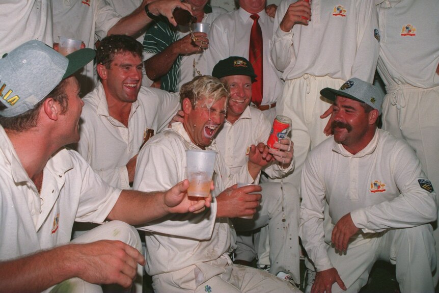 Shane Warne smiles as beer is poured over him in a changing room celebration