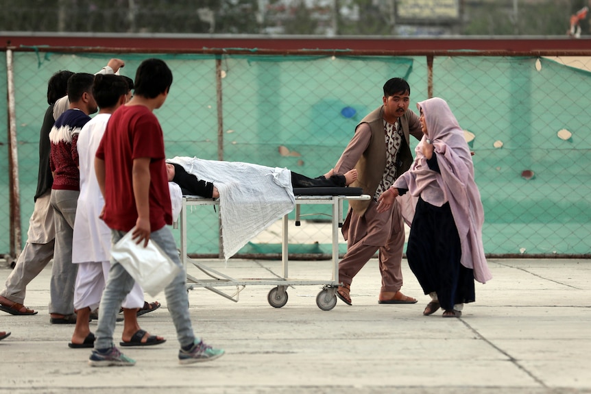 An injured school student is transported to a hospital on a stretcher as her mother walks near by.