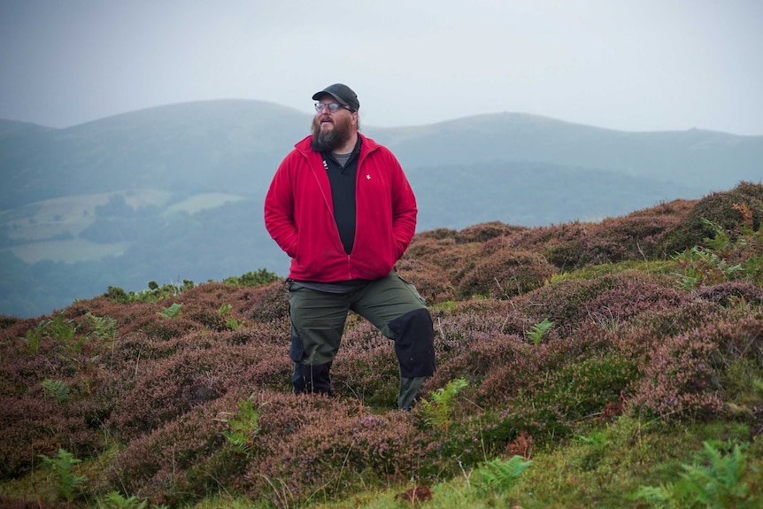 A man in a red jumper standing in a moor surrounded by heather