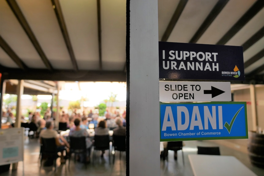 a room is full of older people, who entered through a door with stickers on it supporting Adani and Urannah Dam 