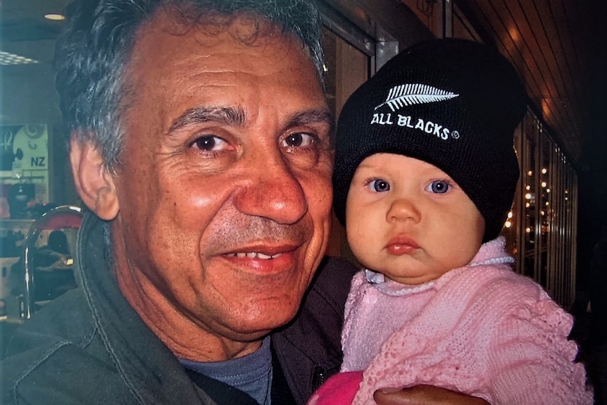 Tight posed shot with man with baby girl wearing an All Blacks woollen hat. Indoors