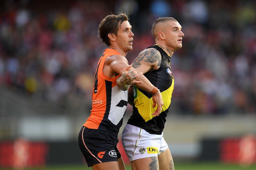 An AFL player is held up from behind by an opponent
