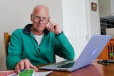 A bald man sits at a table in front of a computer