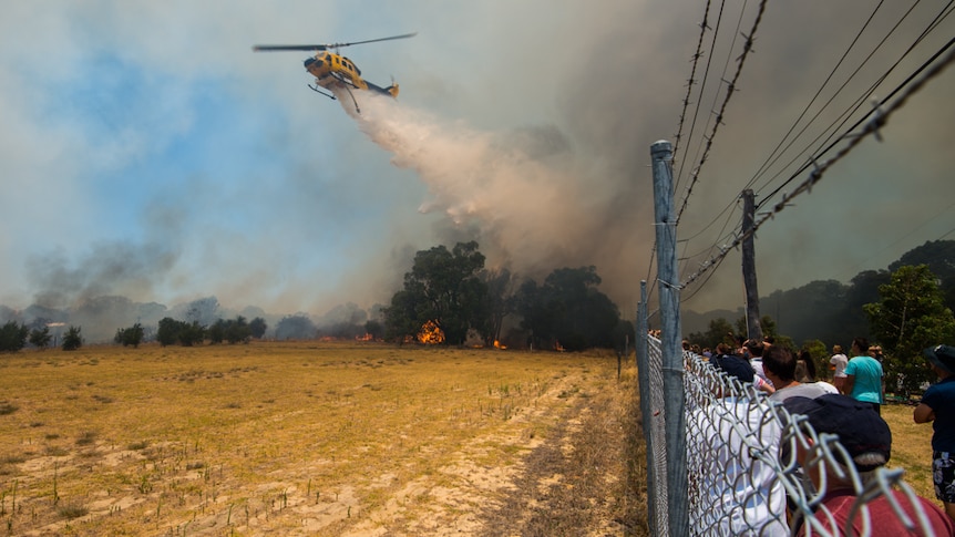 A crowd watches as a helicopter sprays fires in western Perth