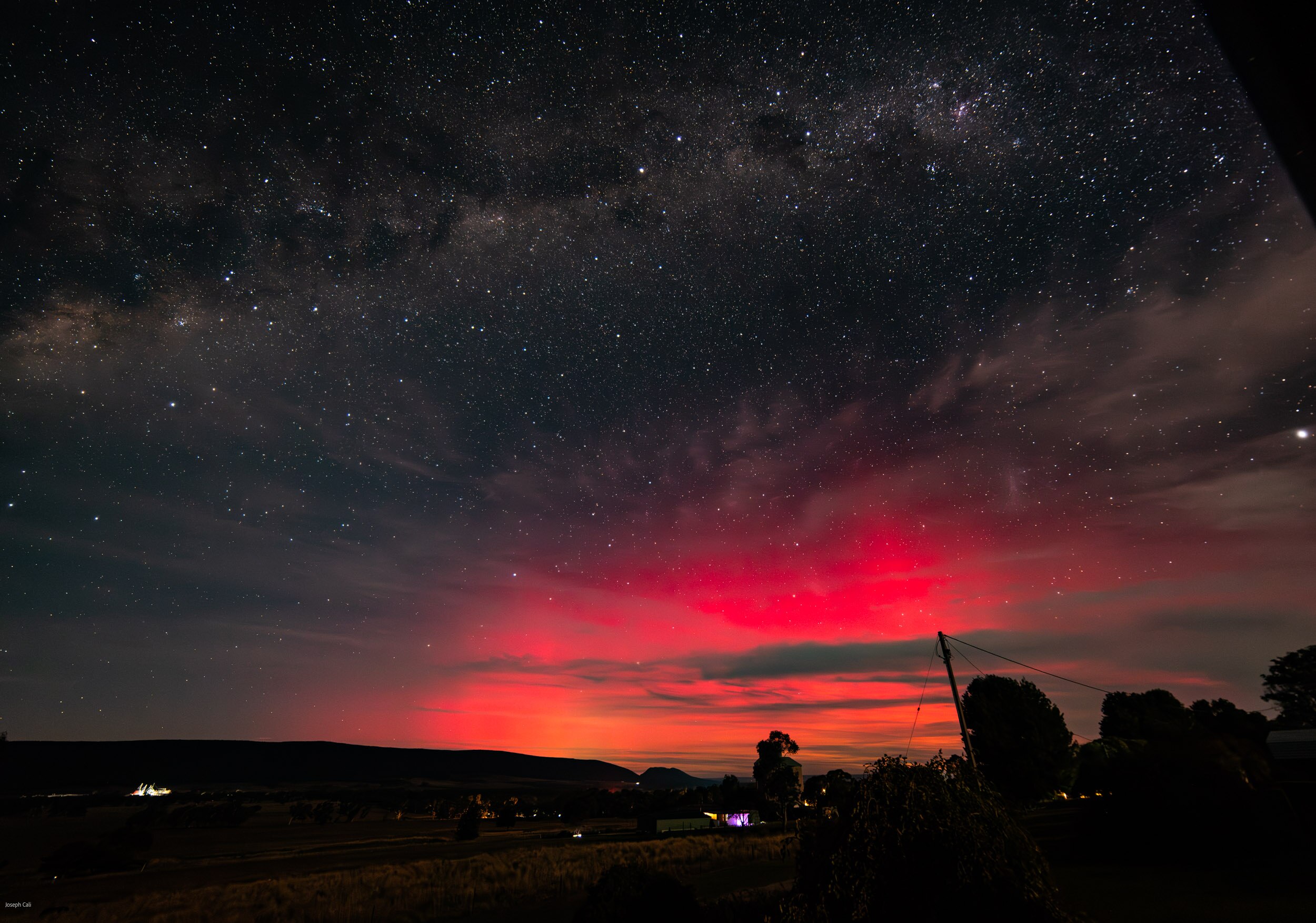 a pink glow in the night sky above a rural plain