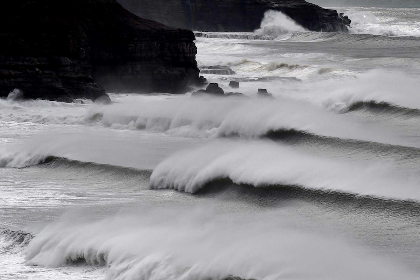 Several sets of huge waves break as they roll in on a rocky coastline.