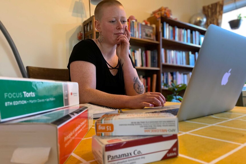 A woman working on a laptop with painkilling medication and law textbooks in the foreground.
