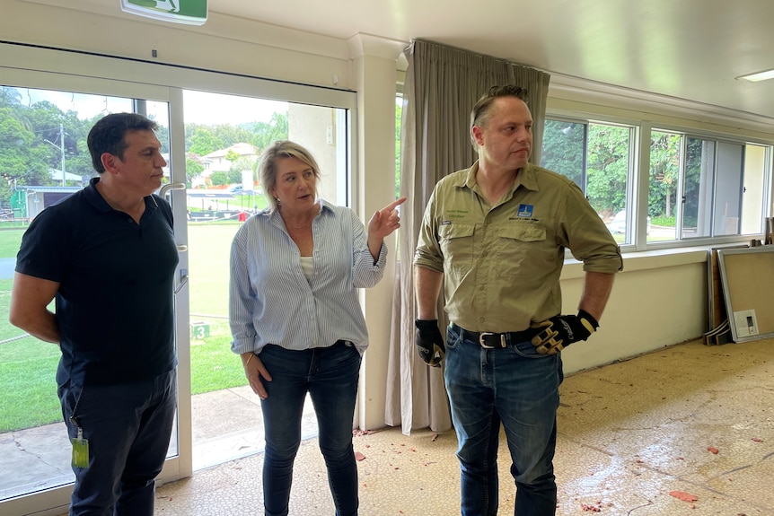 Three people stand in a damaged building looking at something to the right