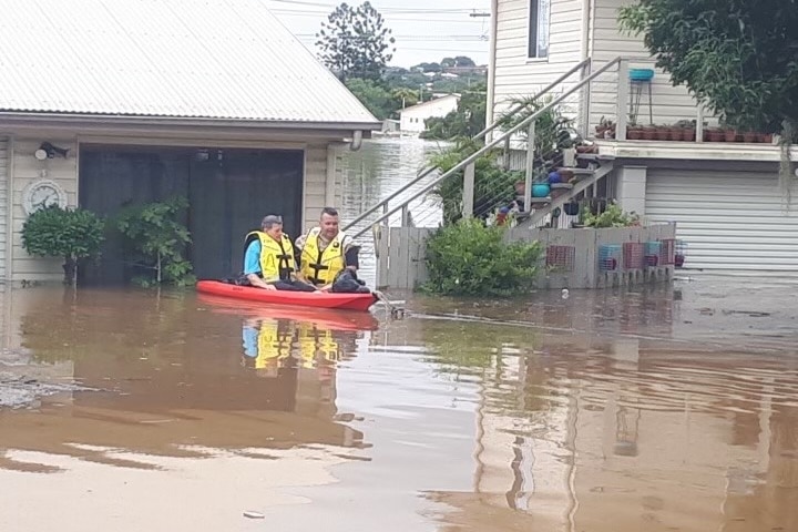 Woman in red canoe with firefighter, in front of flooded home
