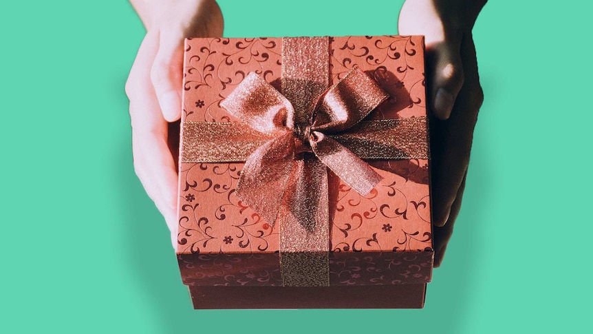 Two hands hold a gift box which is wrapped in bow to depict celebrating your son's first birthday decades after forced adoption.