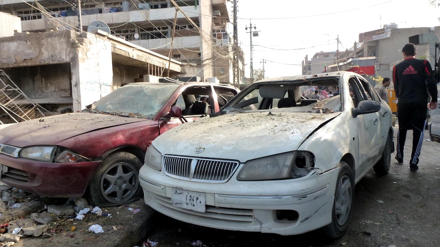 Cars with shattered windows are parked in a street after a wave of attacks in Baghdad.