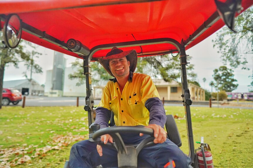 A man smiles while sitting on a ride-on mower.