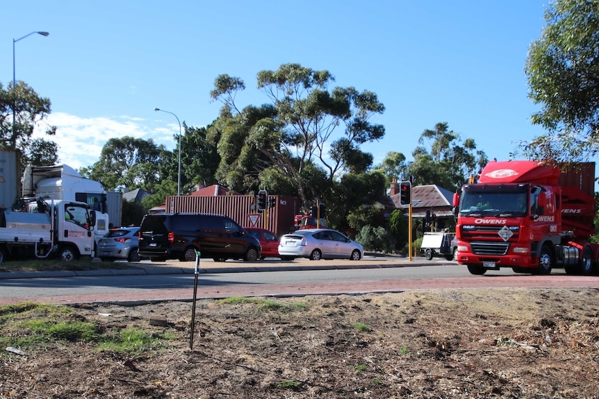 A surbuban highway intersection with cars and several trucks waiting at traffic lights.