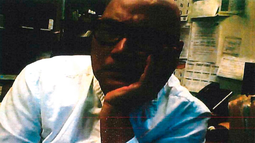 Man wearing glasses and a white shirt sits with chin in hand