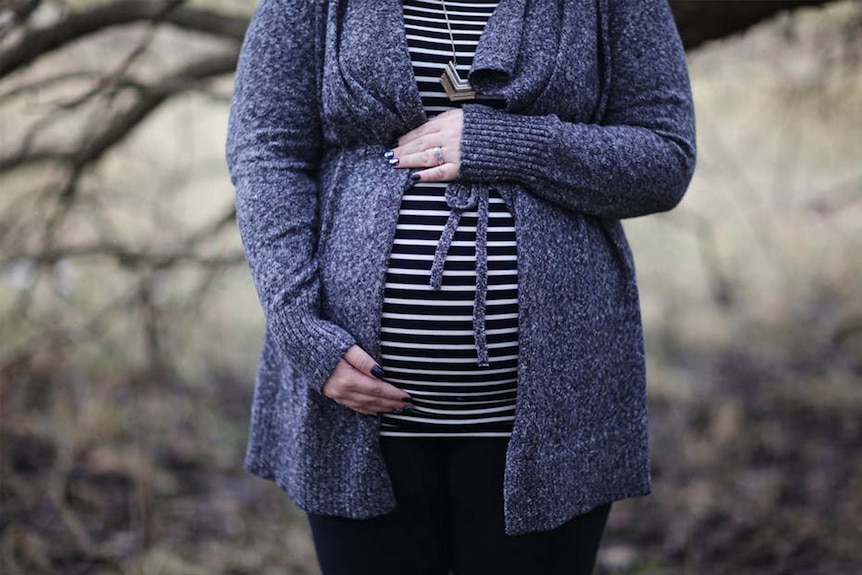 A pregnant woman with her hand on her belly.