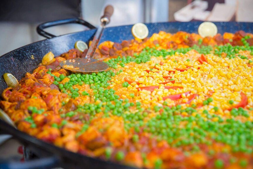A yummy bowl of paella in a pan with rice, chicken and peas.