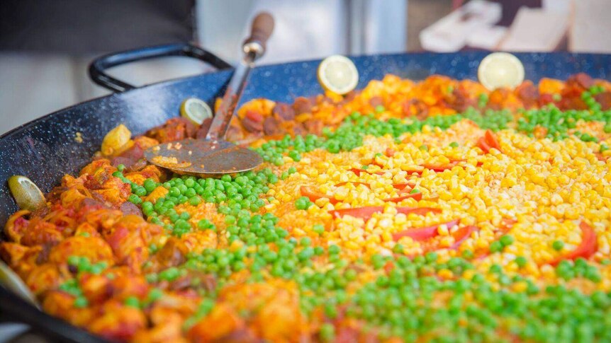 A yummy bowl of paella in a pan with rice, chicken and peas.