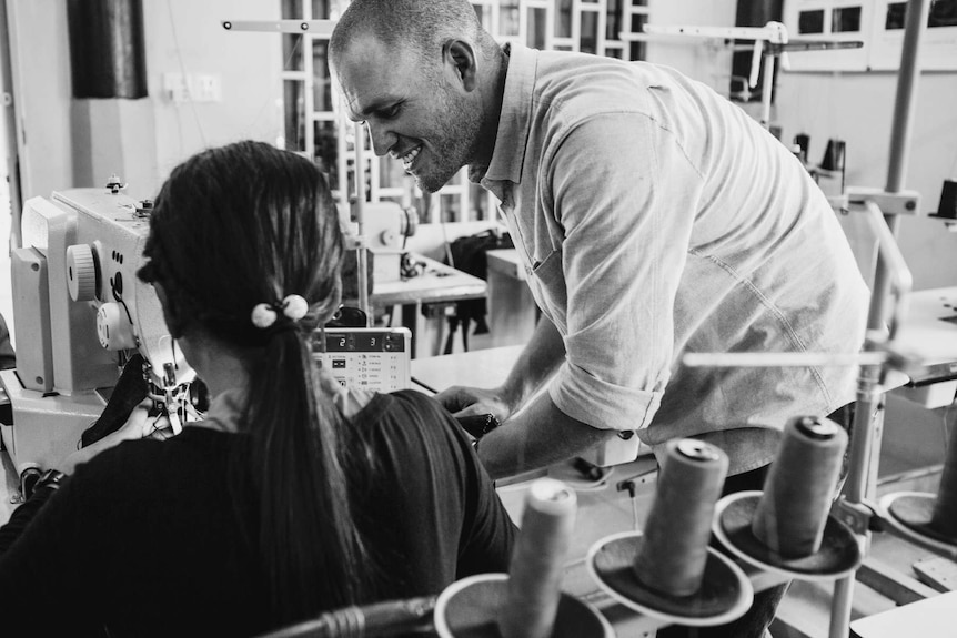 Man teaching a woman on a sewing machine.