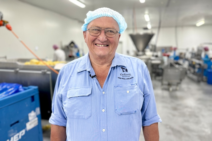 A man smiles for the camera standing on a factory floor.