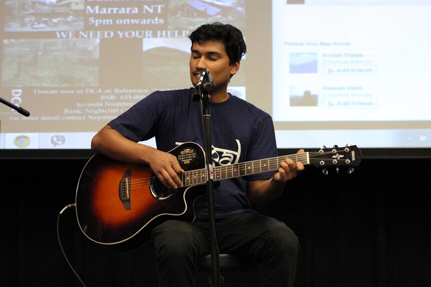 A man sings behind a microphone with a guitar.