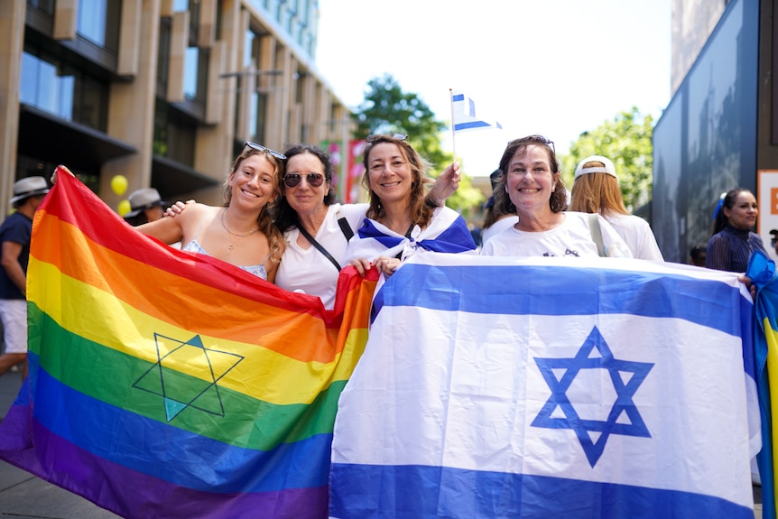 Group of four women hold a rainbow flag with the Star of David, and the Israeli flag