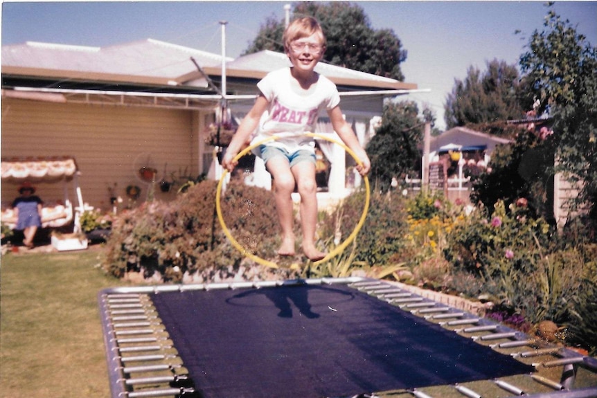 A photo from the 1980s shows a young boy jumping on a trampoline while holding a hula hoop.