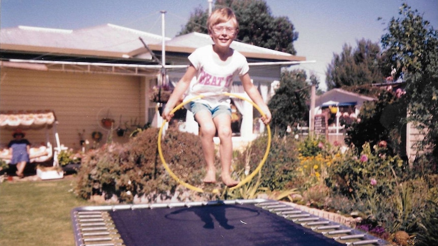 A photo from the 1980s shows a young boy jumping on a trampoline while holding a hula hoop.