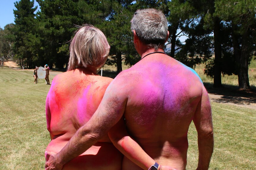 Two people with their backs to the camera, naked covered in coloured dust. 