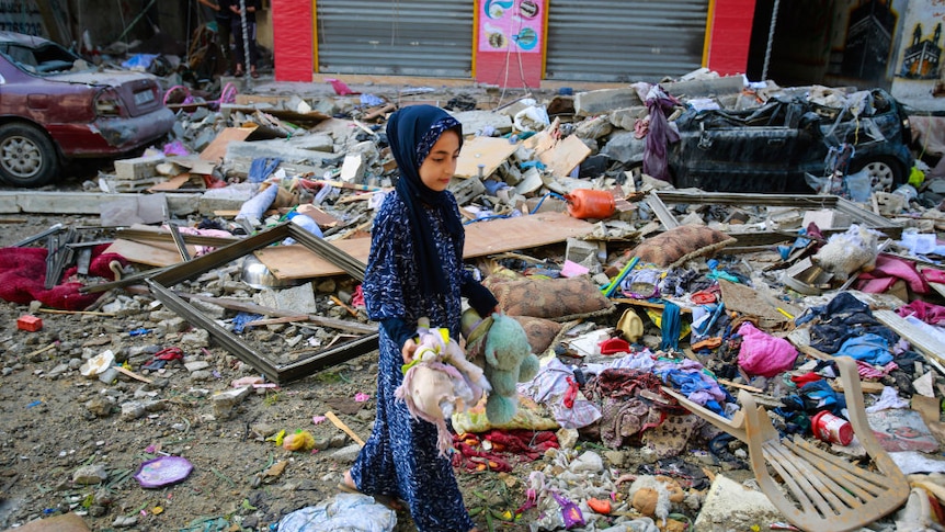 A Palestinian girl holds soft toys as she walks through the rubble of her neighbour's home destroyed by an Israeli airstrike.