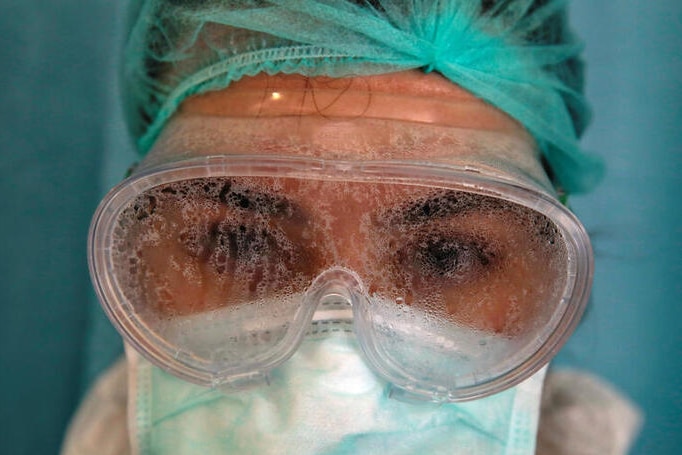 A female health worker in full protective gear with fogged up goggles on