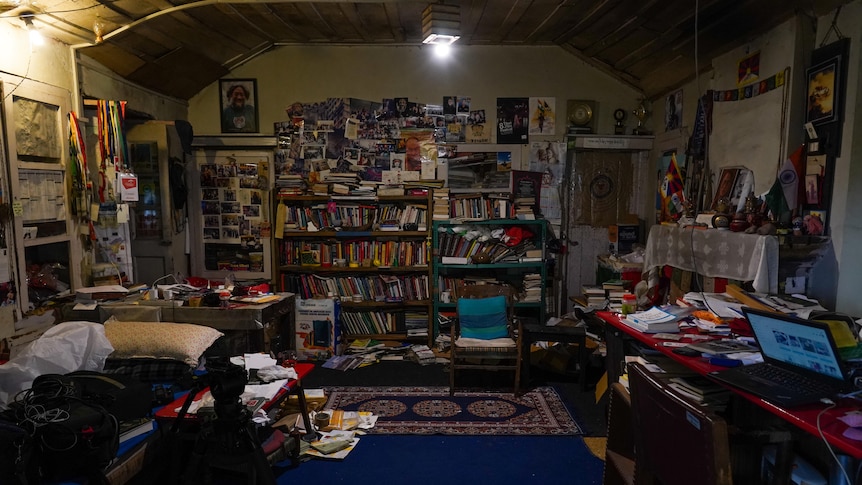 A messy room with book cases stacked full against walls, papers strewn across a desk, and walls filled with art