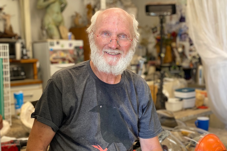 A man smiling at the camera in a busy art studio. 