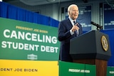 Joe Biden stands at a lectern, pointing, in front of a sign saying CANCELING STUDENT DEBT