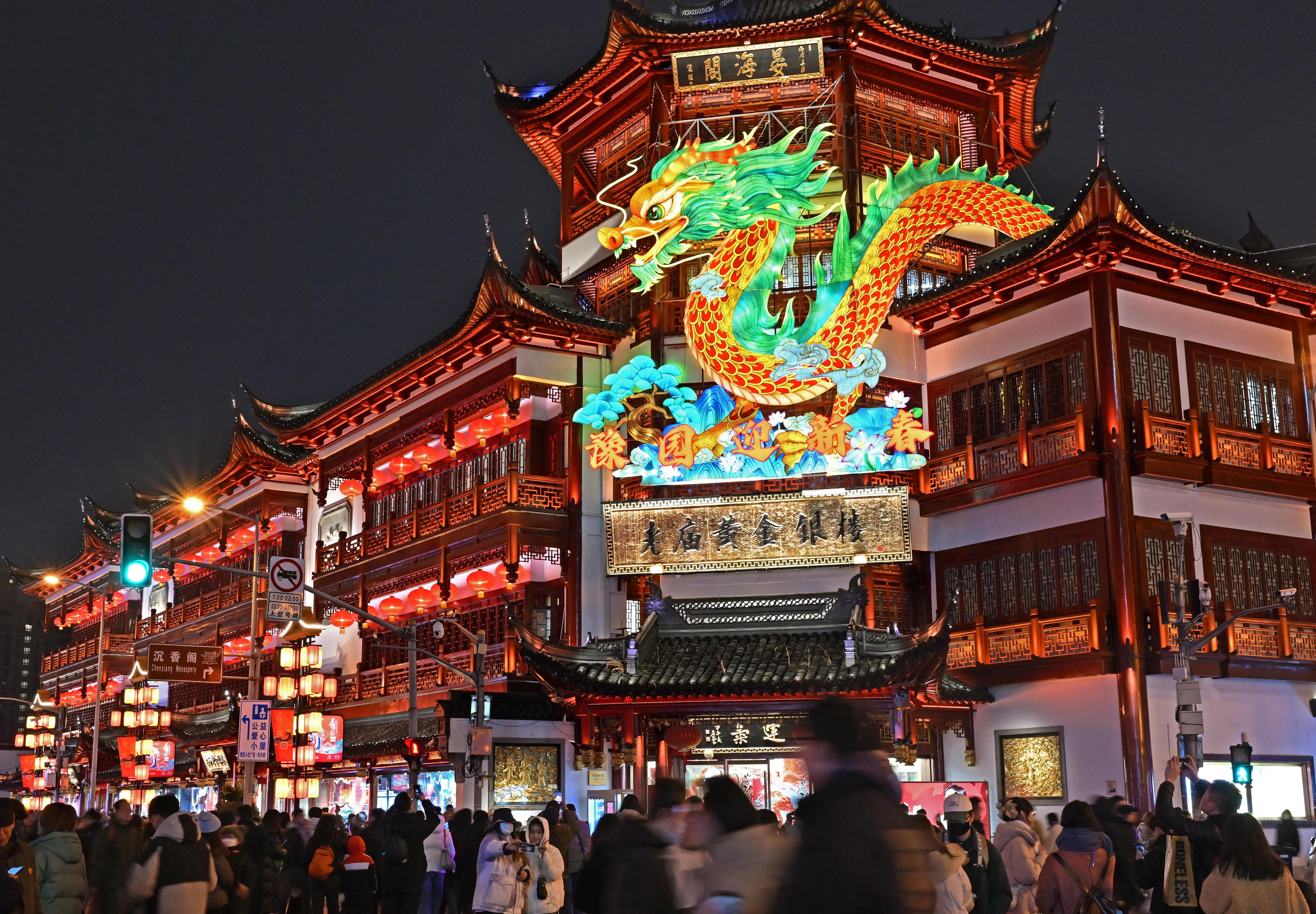 A crowd of people outside a temple with a light up dragon. 