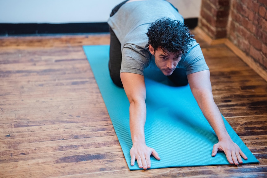 A dark-haired man on his haunches leaning forward onto a floor mat