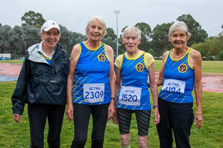 Four women standing together, wearing athletics badges with participant numbers on them.