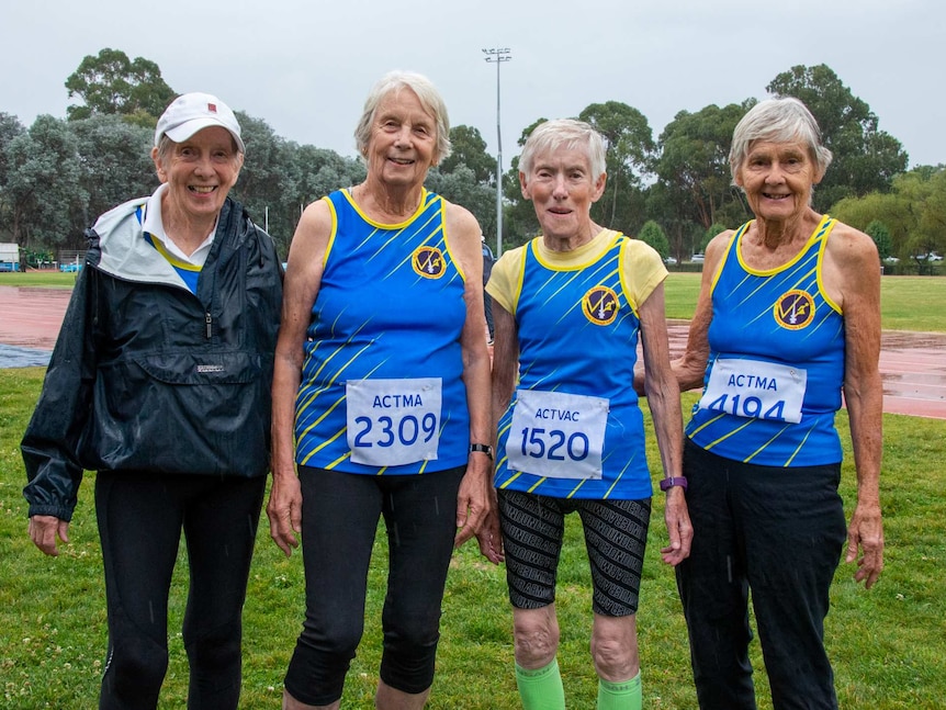 Four women standing together, wearing athletics badges with participant numbers on them.