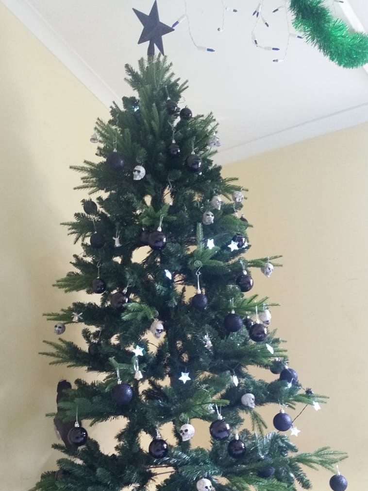 An artificial Christmas tree topped with a black star and decorated with skull ornaments.