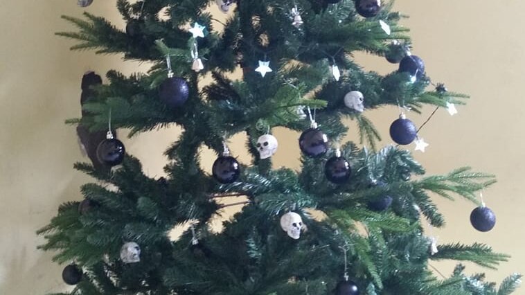 An artificial Christmas tree topped with a black star and decorated with skull ornaments.