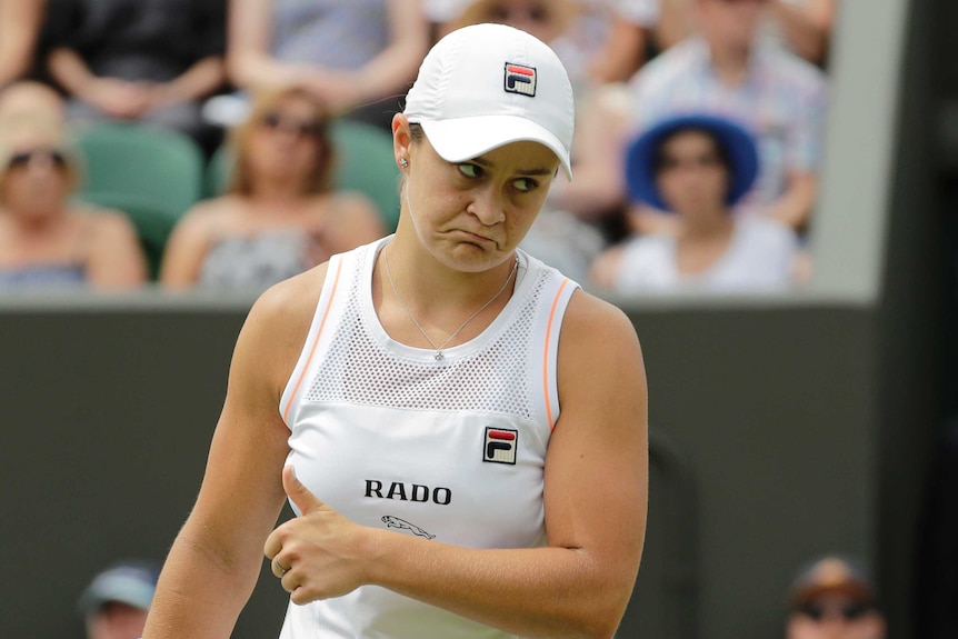 Ash Bart frowns while giving a thumbs on a tennis court