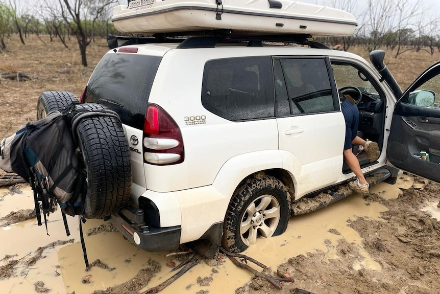 A white 4WD bogged up to its wheels in brown mud