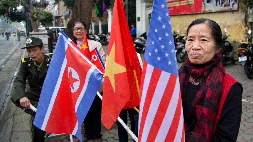 A woman with flags of North Korea, U.S and Vietnam stands on the street.