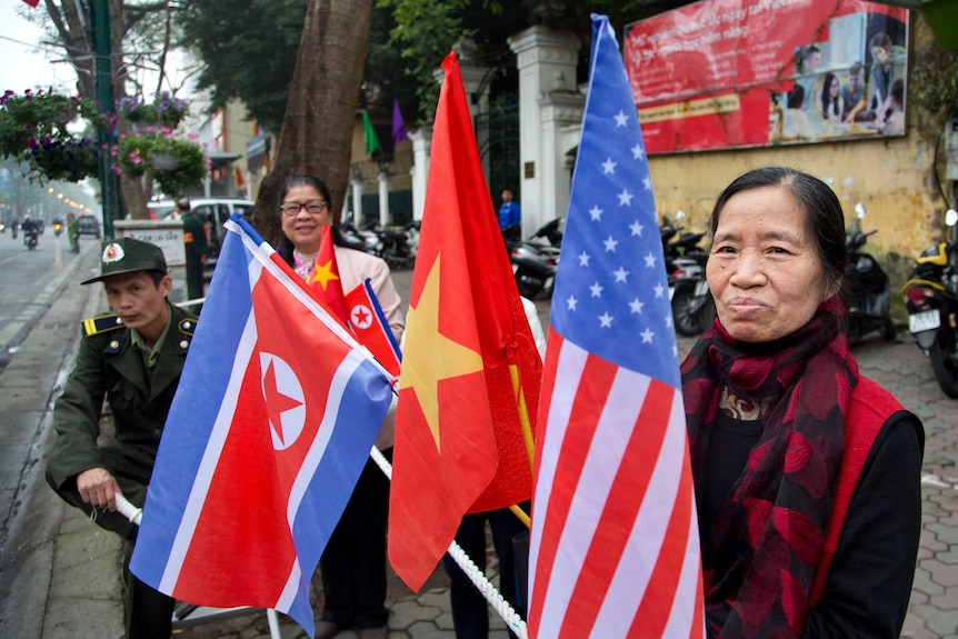 A woman with flags of North Korea, U.S and Vietnam stands on the street.