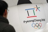 A man walks by the official emblem of the 2018 Pyeongchang Olympic Winter games. It is a multicolour box and asterisks shape.