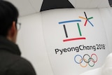 A man walks by the official emblem of the 2018 Pyeongchang Olympic Winter games. It is a multicolour box and asterisks shape.