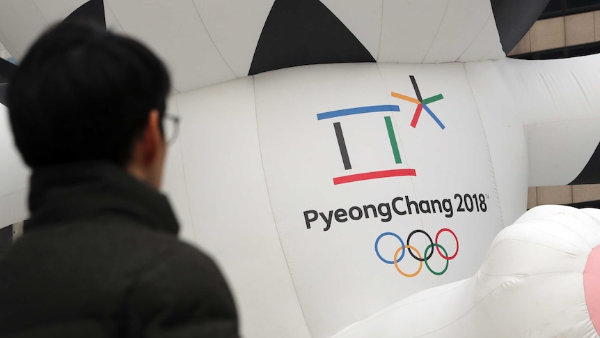 A man walks by the official emblem of the 2018 Pyeongchang Olympic Winter games. It is a multicolour box and asterisks shape.