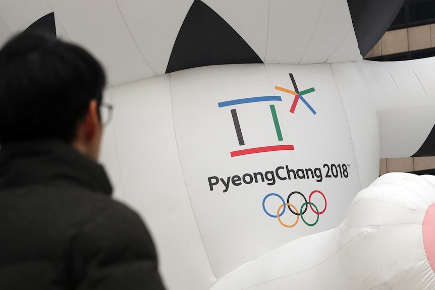 A man walks by the official emblem of the 2018 Pyeongchang Olympic Winter games. It is a multicolour box and asterisks shape.